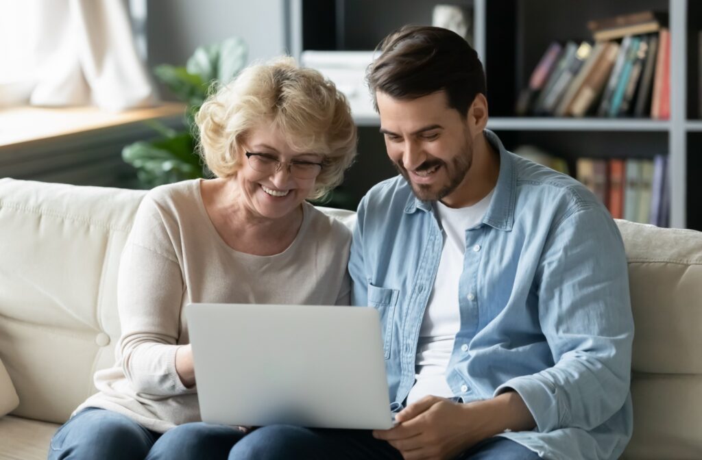 An adult child and their senior parent look at memory care communities on the computer.