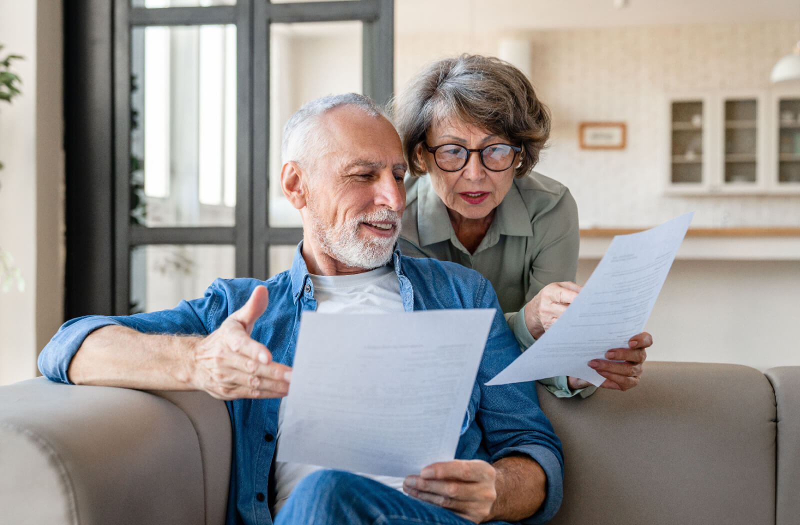 A married couple reviewing paperwork together on the couch and comparing their numbers for their retirement budget.