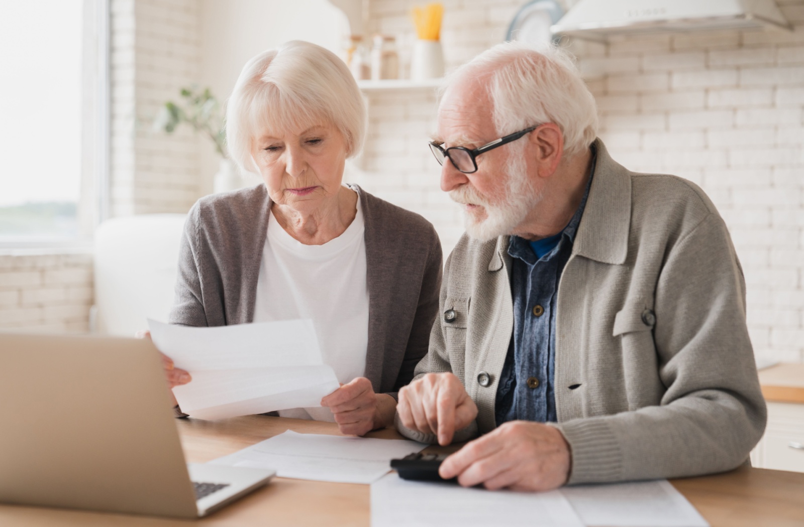 An older married couple working through paperwork with a calculator to budget ahead for retirement.